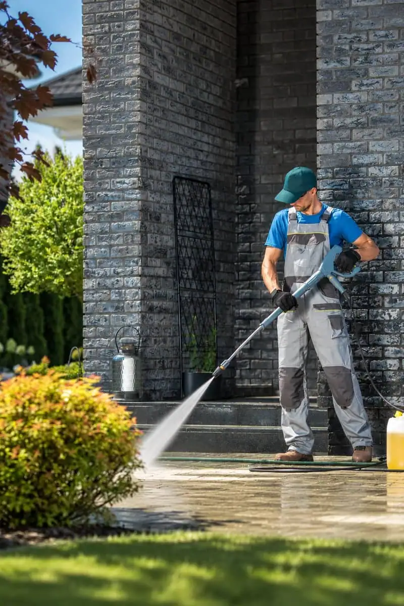 A tech pressure washing a brick patio
